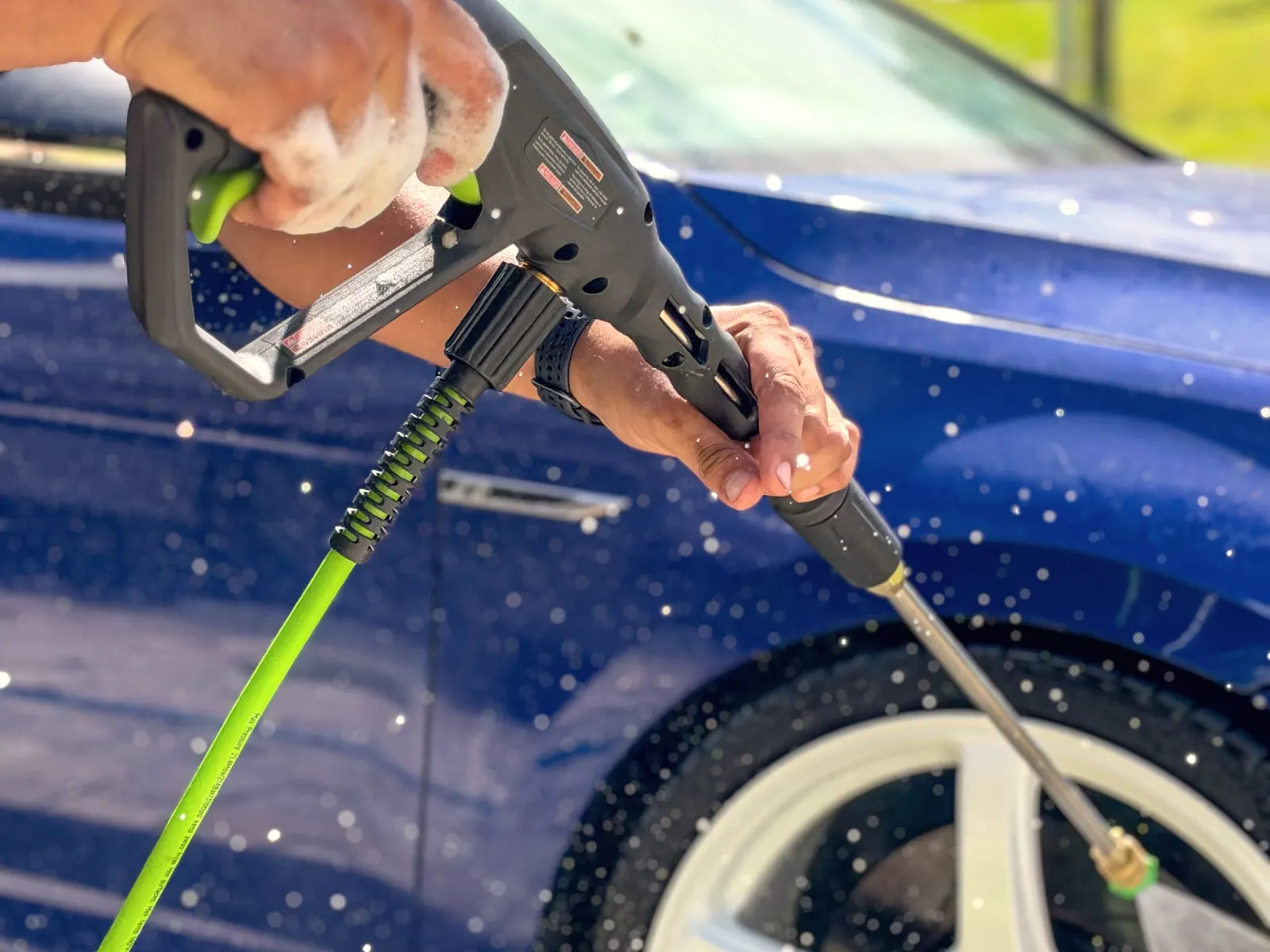 Gloved hand pressure washing a wheel during a mobile detail